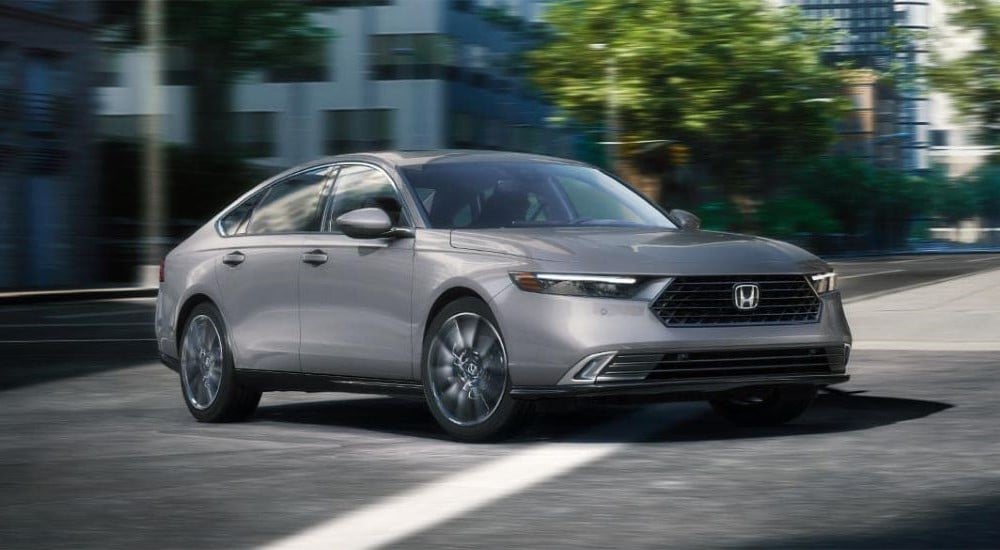 A grey 2024 Honda Accord Touring Hybrid driving in a city intersection after visiting a Honda dealer near Bennington.