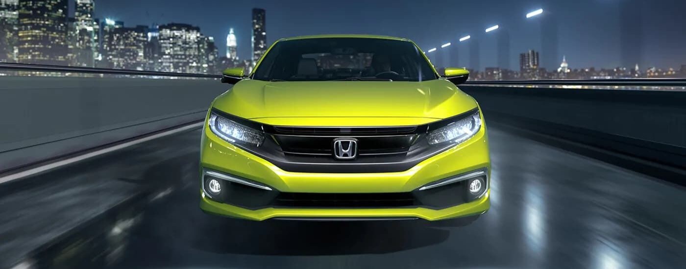 Front angle view of a neon yellow 2019 Honda Civic Touring driving over a bridge.