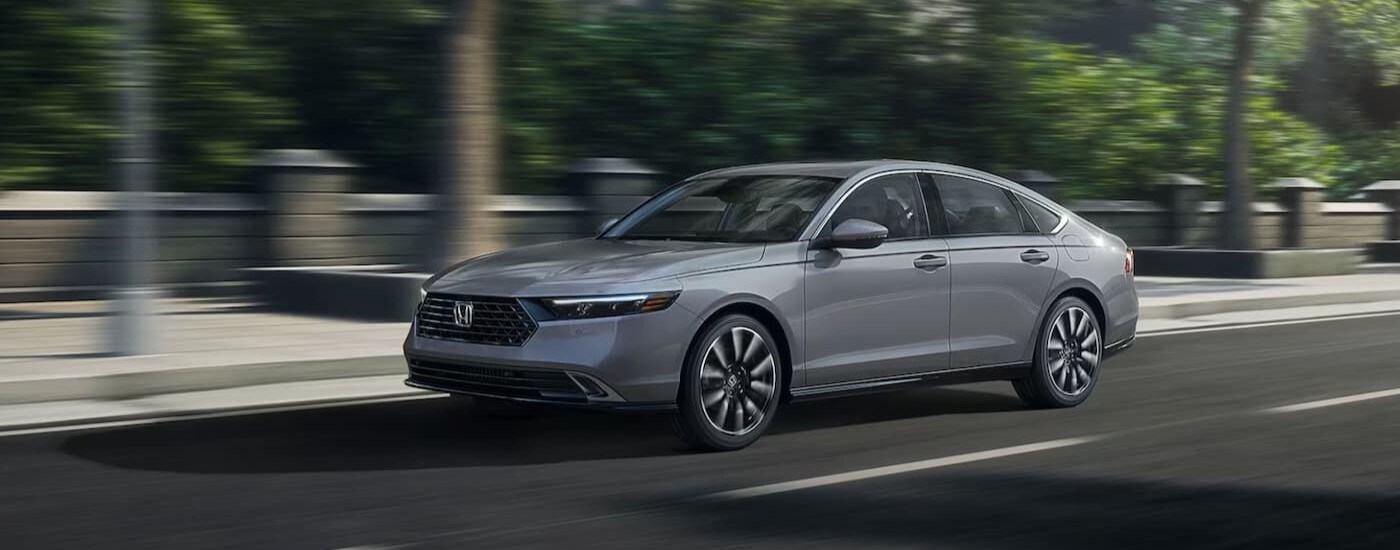 A gray 2025 Honda Accord Touring Hybrid is shown driving on a city street.