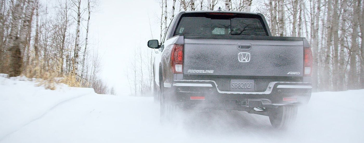 A grey 2020 Honda Ridgeline is shown from the rear driving on a snowy trail.