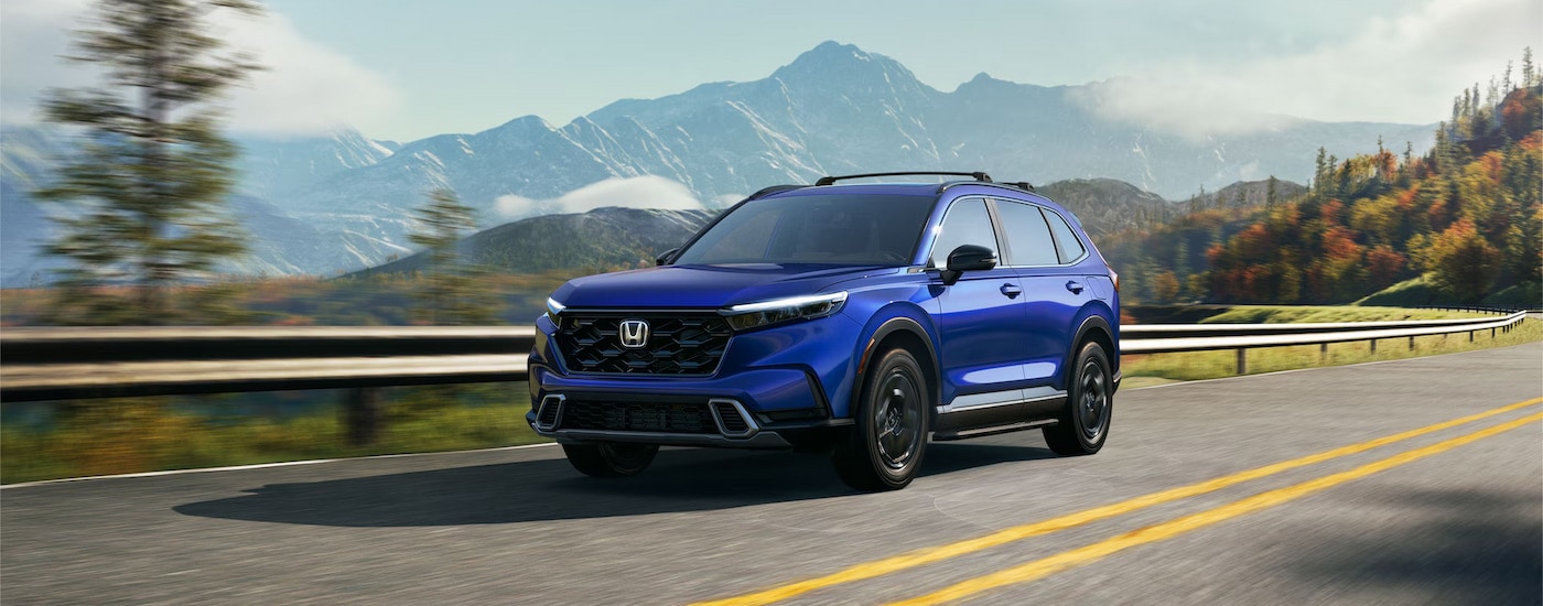 A blue 2024 Honda CR-V Sport Touring Hybrid driving on a mountain highway.