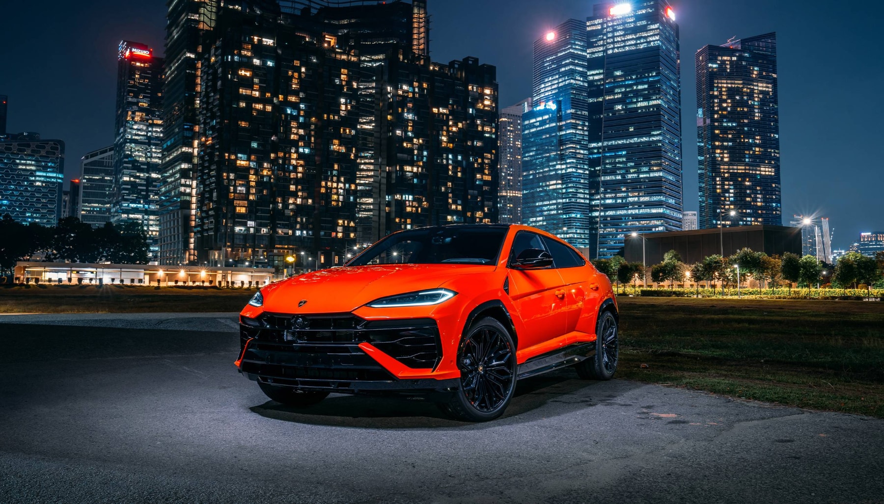 Orange Lamborghini Urus parked in front of a city