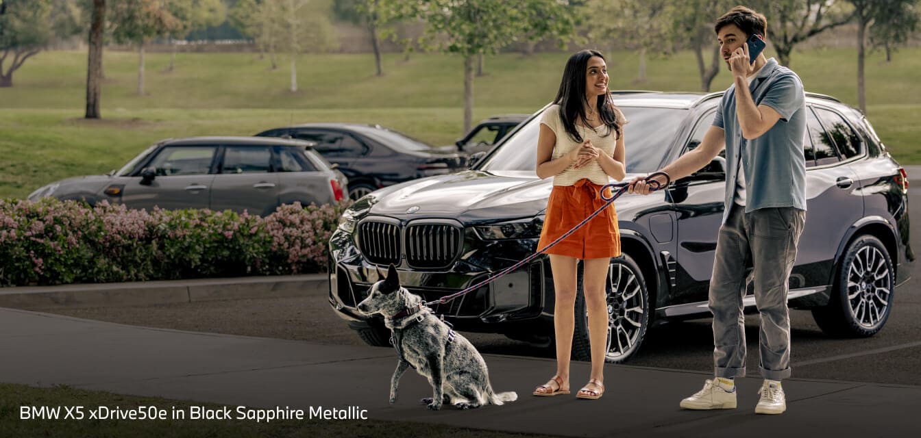 A couple and their dog in front of a BMW X5 xDrive50e in Black Sapphire Metallic