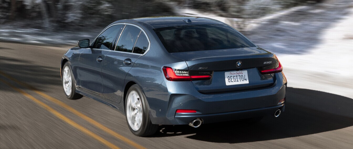 2026 BMW 330i xDrive in blue driving on a road with a blurry snow background