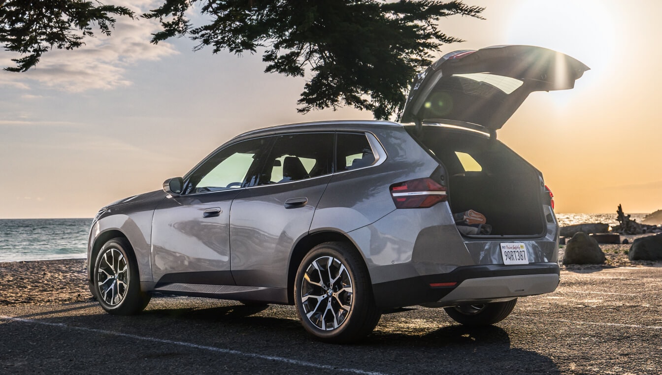 Rear three-quarter view of a new 2025 BMW X3 parked at the beach with an open liftgate