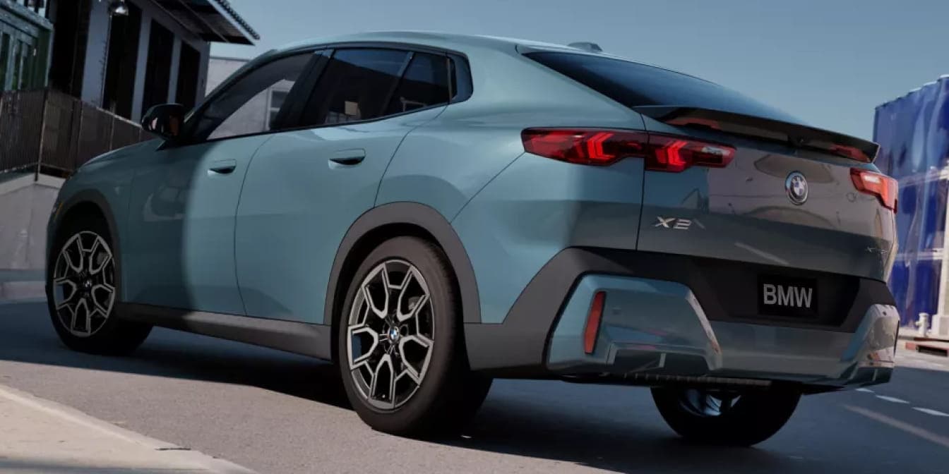 A light blue BMW X2 SUV shown from a rear three-quarter angle driving through an urban street.