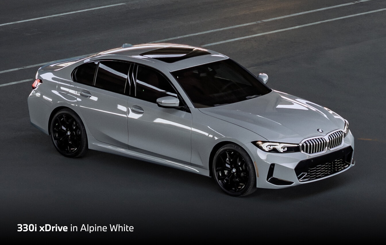2026 BMW 330i xDrive in White, front three-quarter overhead view on a city road.