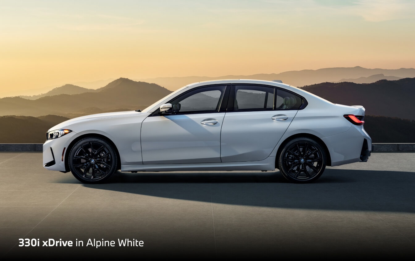 2026 BMW 330i xDrive in Alpine White, side profile on a terrace with mountains at sunset.