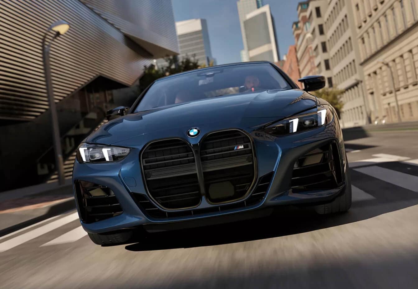 A front view action shot of a dark blue BM4 4-Series M4 Sedan driving down a city street.