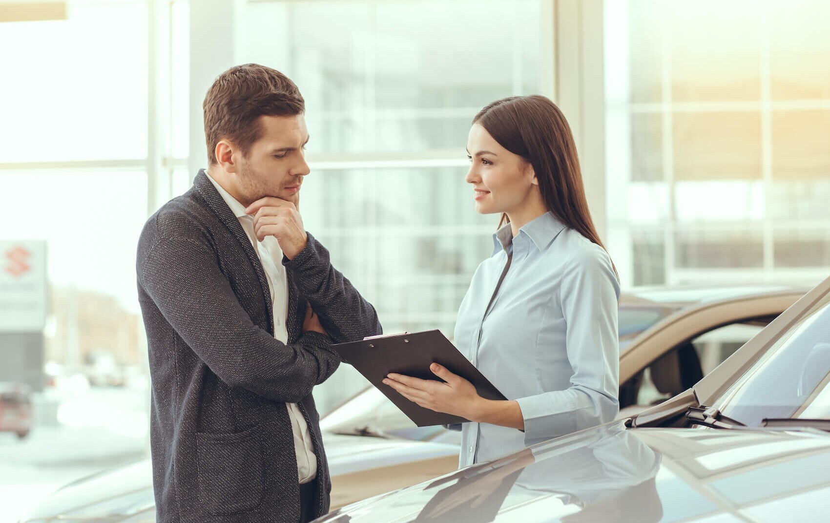 Sales person speaking to customer over paperwork next to car