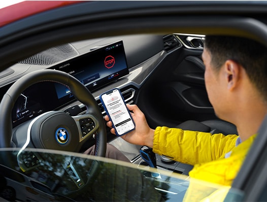  Man holds smartphone with screen visible while sitting in driver’s seat of a BMW vehicle.