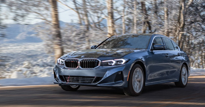 Blue BMW sedan driving past snow-covered trees