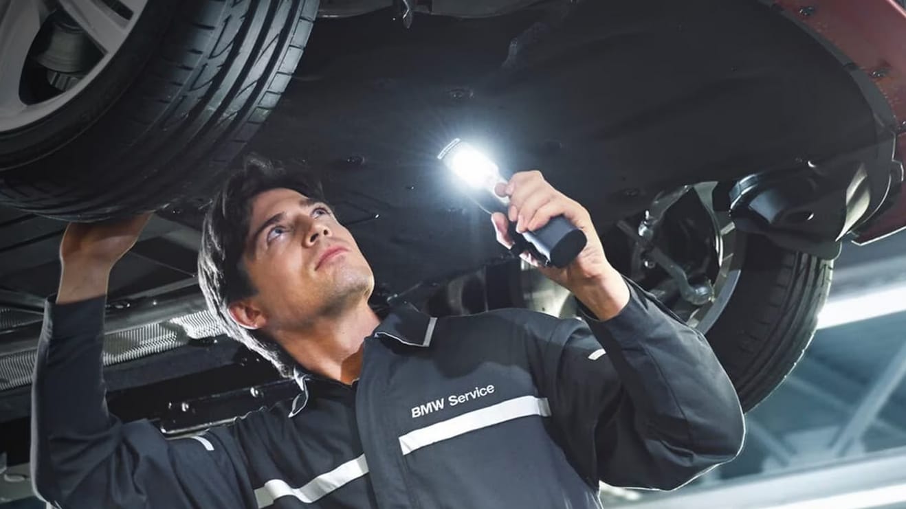 A service technician inspecting the underside of a BMW vehicle.