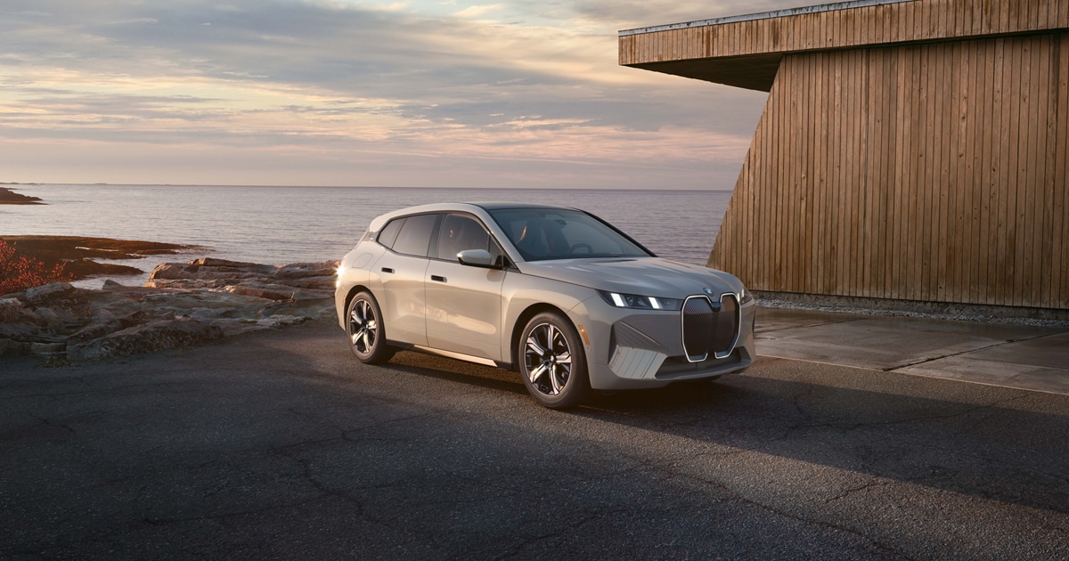 The BMW iX parked by an oceanside home during sunset.