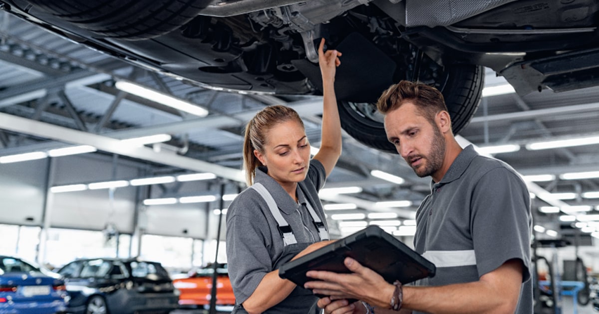 Two BMW service technicians performing a diagnosis on a BMW vehicle for maintenance at a BMW service center.