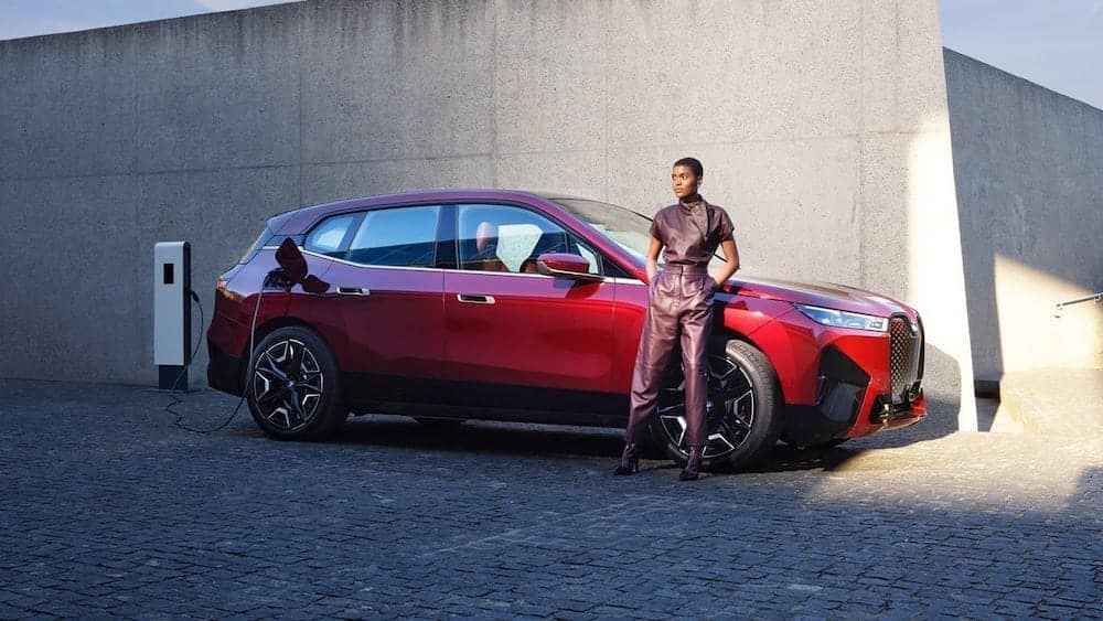 Red BMW iX Charging with a woman standing next to it - Pre-Order from BMW of Monterey today!