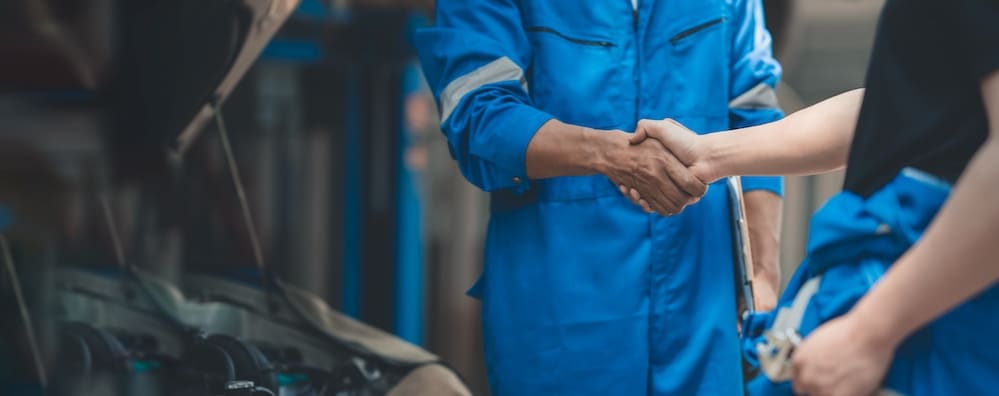Two service technicians shaking hands in front of a vehicle’s open hood