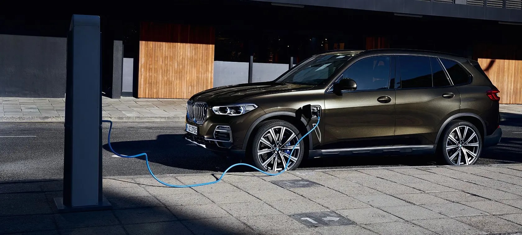 Vue latérale du BMW X5 en recharge de batterie sur une borne électrique extérieure.