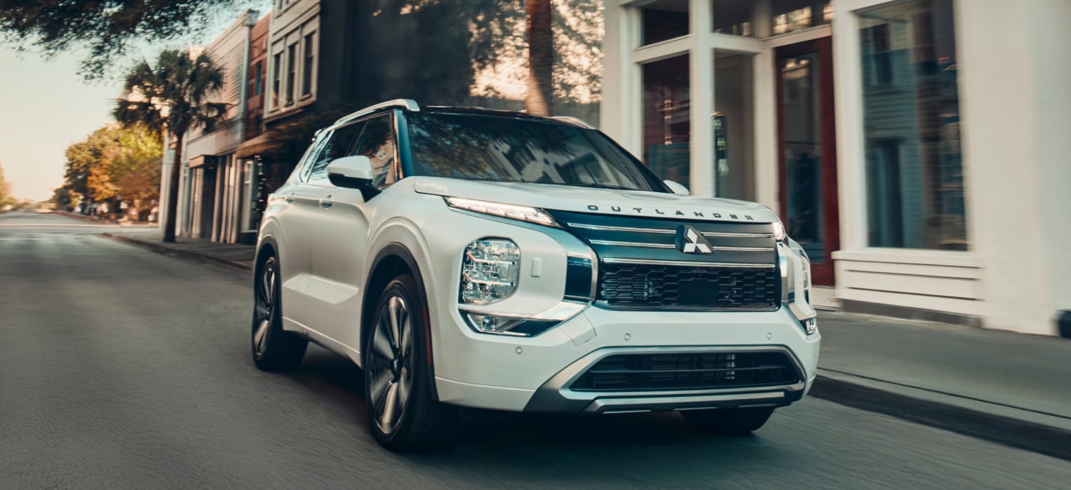 A%20white%20Mitsubishi%20Outlander%20SUV%20driving%20on%20a%20city%20street.png