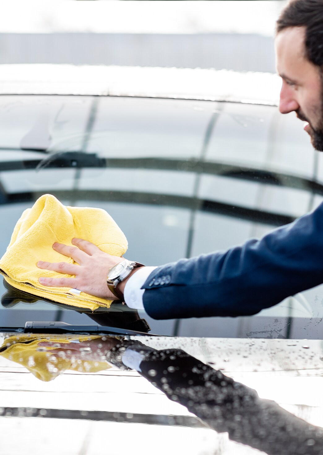 Remove Dead Bugs From Front of Cars at Bobby Rahal Acura in Mechanicsburg, PA | Man in navy blue suit wipping his car windshield with yellow cloth 