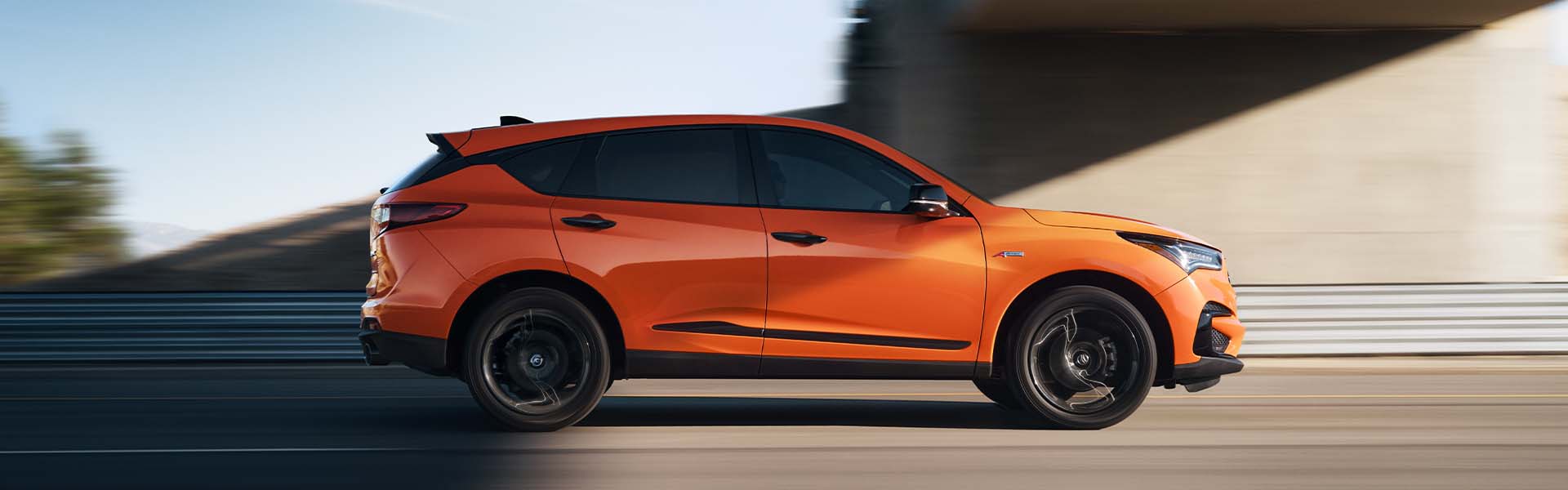 Model Features of the 2021 Acura RDX at Bobby Rahal Acura | Profile View of Orange 2021 Acura RDX Driving Under Underpass