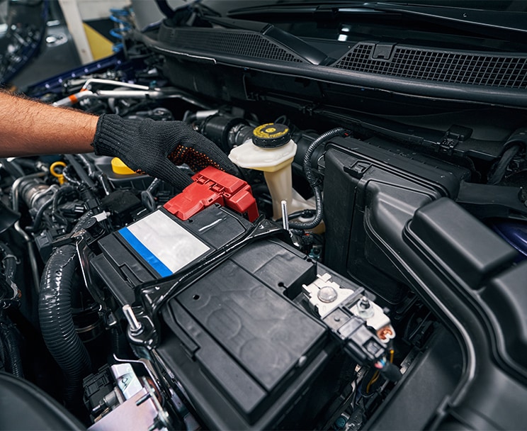 Everything You Need to Know about Your Car Battery at Bobby Rahal Acura | Person with black gloves inspecting battery located in the engine bay 