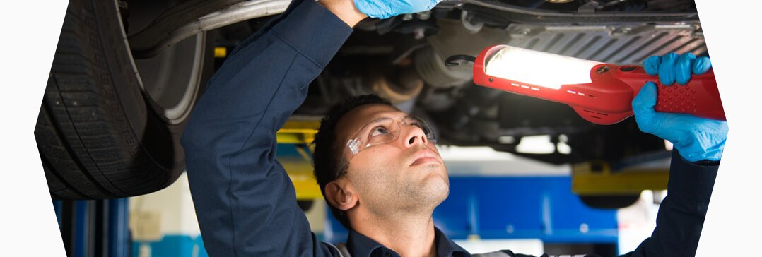 How to prepare your Acura for the winter season in Mechanicsburg, PA at Bobby Rahal Acura | Close-up of Bobby Rahal Acura Technician inspecting under car on lift with big light