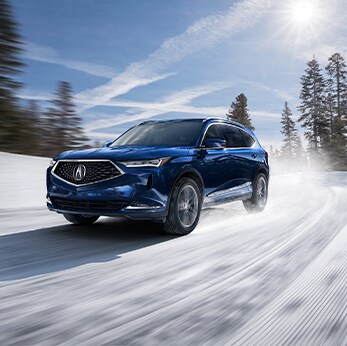 How to prepare your Acura for the winter season in Mechanicsburg, PA at Bobby Rahal Acura | Dark blue MDX driving fast on snowy turn in woods