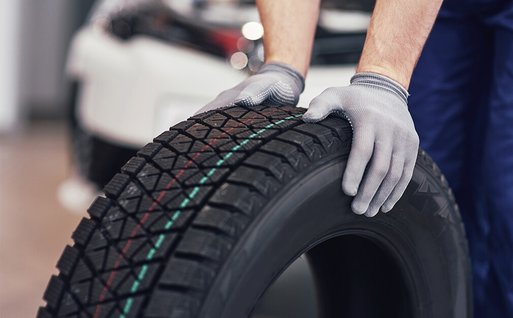 Learn Maintenance Warning Signs at Bobby Rahal Acura in Mechanicsburg, PA | Person with grey gloves is rolling new tire on the floor 
