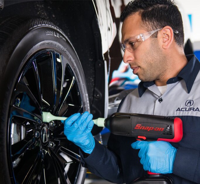 Acura Maintenance At Bobby Rahal Acura in Mechanicsburg, PA | Mechanic in Acura uniform is tightening the lug nuts of a wheel by using a black and red Cordless Impact Wrench 