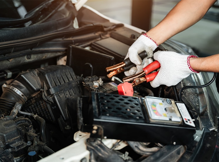 Everything You Need to Know about Your Car Battery at Bobby Rahal Acura |  Man with white gloves testing out the battery life by holding and using a battery volt tester