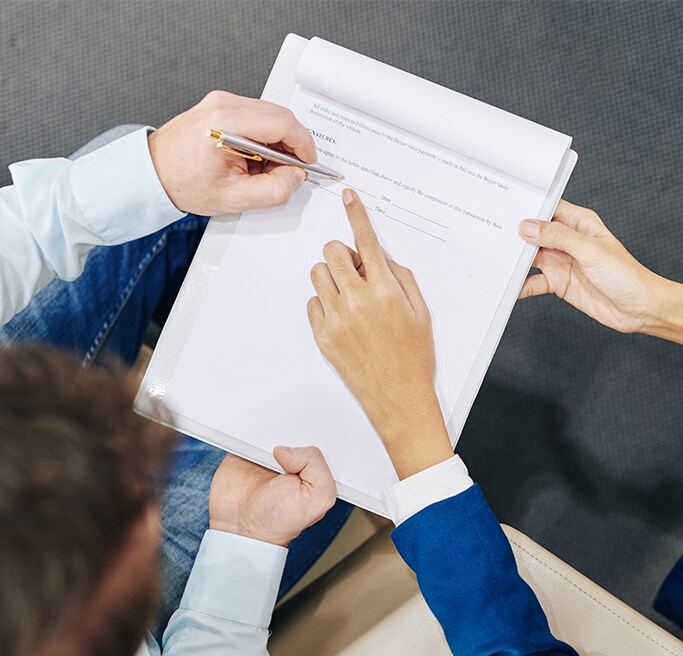 Vehicle Warranty Information at Bobby Rahal Acura in Mechanicsburg, PA | One persons hand pointing to paperwork on where to sign and another persons hand with a pen signing paperwork