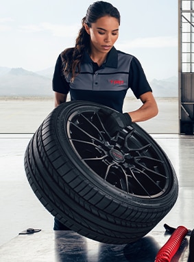 ToyotaCare At Bobby Rahal Toyota in Mechanicsburg, PA | Woman wearing a Toyota TRD work shirt while picking up a black wheel with a new tire