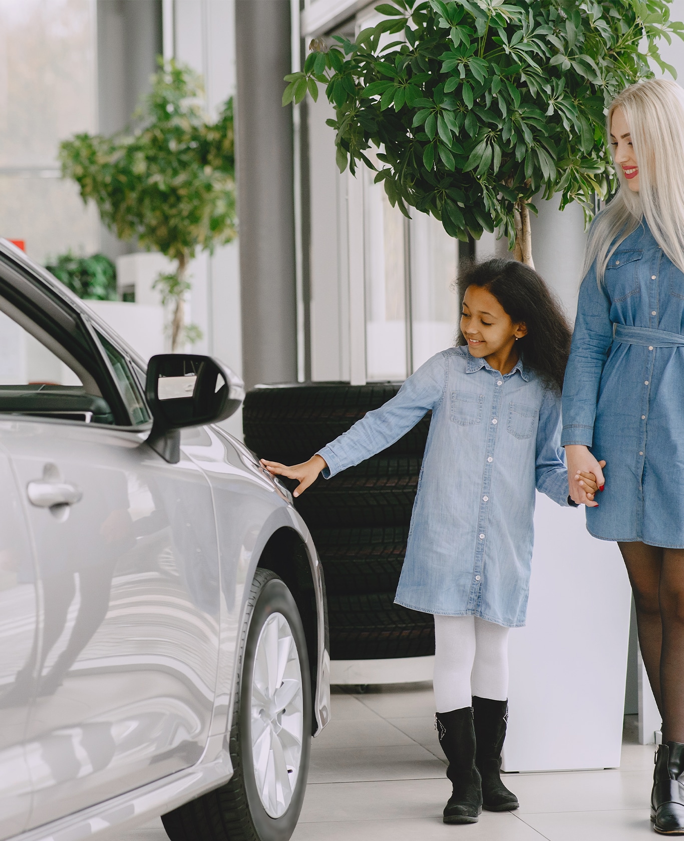 Best Time To Buy At Bobby Rahal Toyota in Mechanicsburg, PA | Woman on the right is holding hands with her daughter while she is touching a new silver car on the left side 