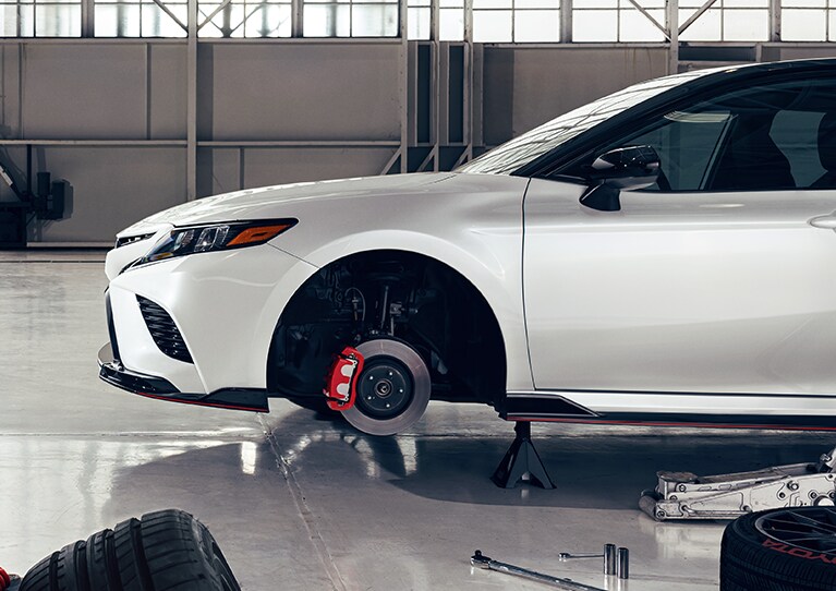 Brake replacement and Safety at Bobby Rahal Toyota | White Toyota Camry with tires off and with red brake calipers 