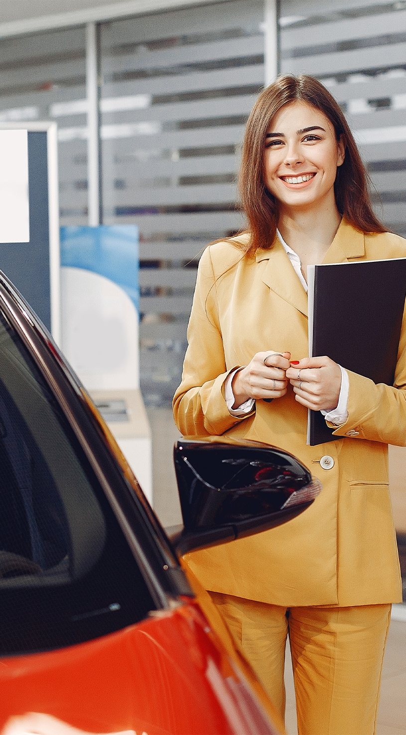 When to Trade In Your Car | Bobby Rahal Toyota in Mechanicsburg, PA | Woman in yellow suit is holding a black folder while standing beside a red vehicle 