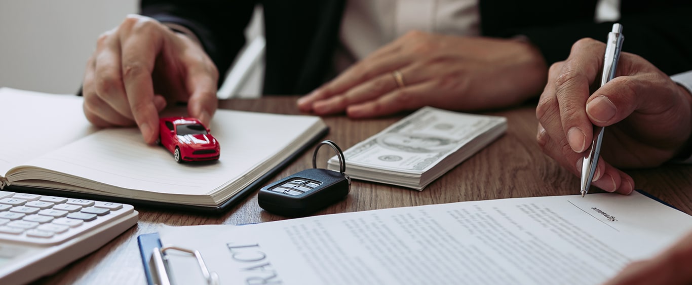 Vehicle Warranty Information at Bobby Rahal Toyota in Mechanicsburg, PA | Person signing paperwork while another person has the keys and toy car model in front of them