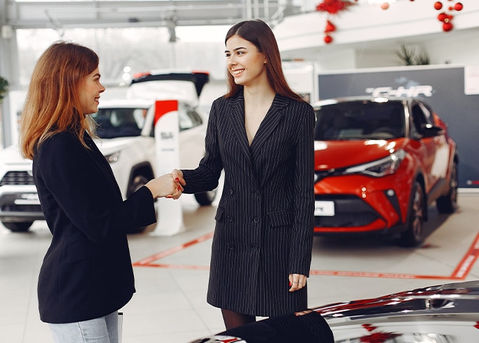 When to Trade In Your Car | Bobby Rahal Toyota in Mechanicsburg, PA | Woman in black suit on the right side is shaking hands with another woman in black blazer, with a red and white vehicle behind them