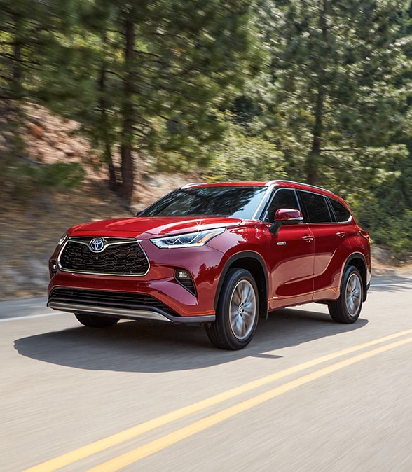 Model Features of the 2022 Toyota Highlander Hybrid at Bobby Rahal Toyota | Red 2022 Highlander Hybrid Driving Down Wooded Road