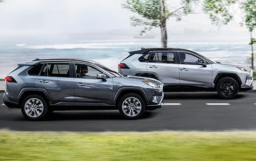 Model Features of the 2021 Toyota RAV4 at Bobby Rahal Toyota | Two RAV4's driving fast past ocean