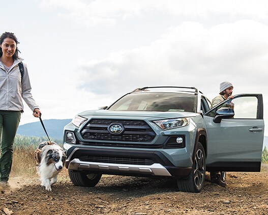 Model Features of the 2021 Toyota RAV4 at Bobby Rahal Toyota | RAV4 on dirt road with hikers and dog