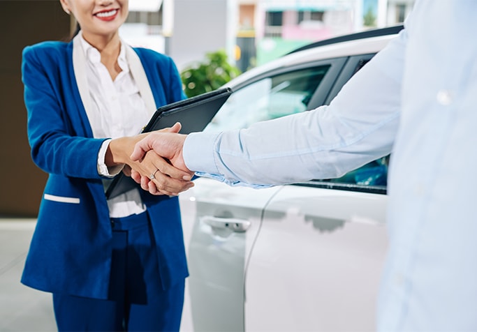 Vehicle Registration Taxes and Fees at Bobby Rahal Toyota in Mechanicsburg, PA | Man in a light blue shirt on the right is shaking hands with a women in blue suit on the left side