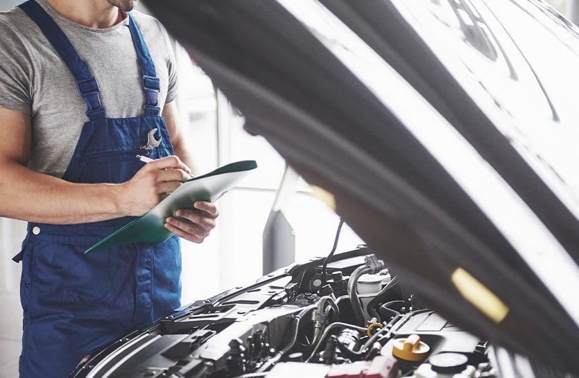 Everything You Need to Know about Your Car Battery at Bobby Rahal Toyota | Man in blue uniform inspecting engine bay with a paper work in his hands 