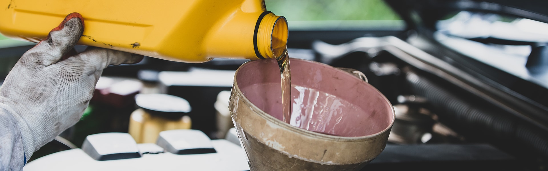 Benefits of Changing Your Toyota’s Oil at Bobby Rahal Toyota in Mechanicsburg | Toyota technician under the hood of a car pouring oil into the filler tube of an engine