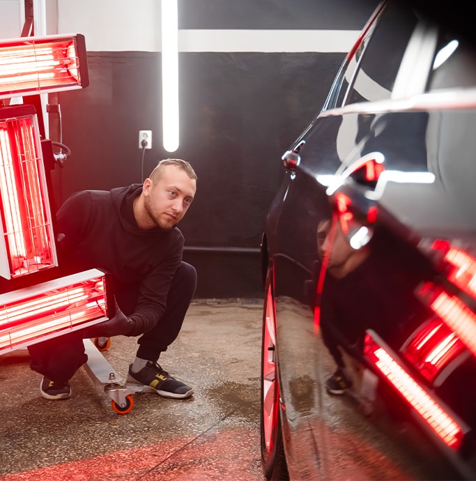 What is Paintless Dent Repair? | Bobby Rahal Toyota | Man in all black outfit adjusting red lights to appear on the black car dents