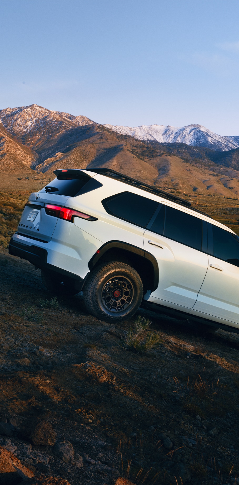 2023 Toyota Sequoia at Bobby Rahal Toyota in Mechanicsburg, PA | Rear of a white 2023 Toyota Sequoia TRD driving down a hill with views of the mountains behind it 