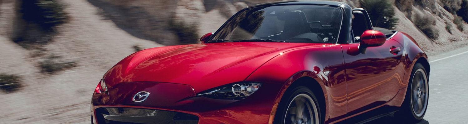 A red 2019 Mazda Miata MX-5 Sport driving fast down a mountain road