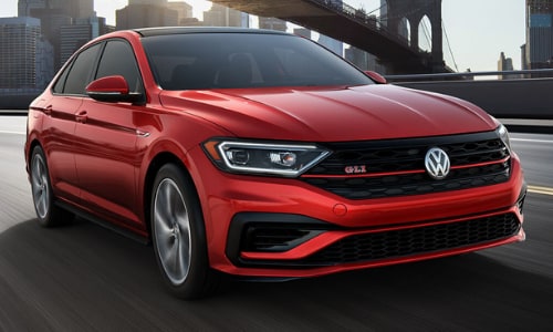2020 Volkswagen Jetta GLI performance sedan in red driving down a highway under bridge city scene