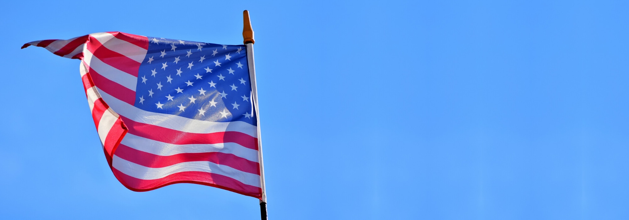 American Flag blowing in the wind blue sky behind
