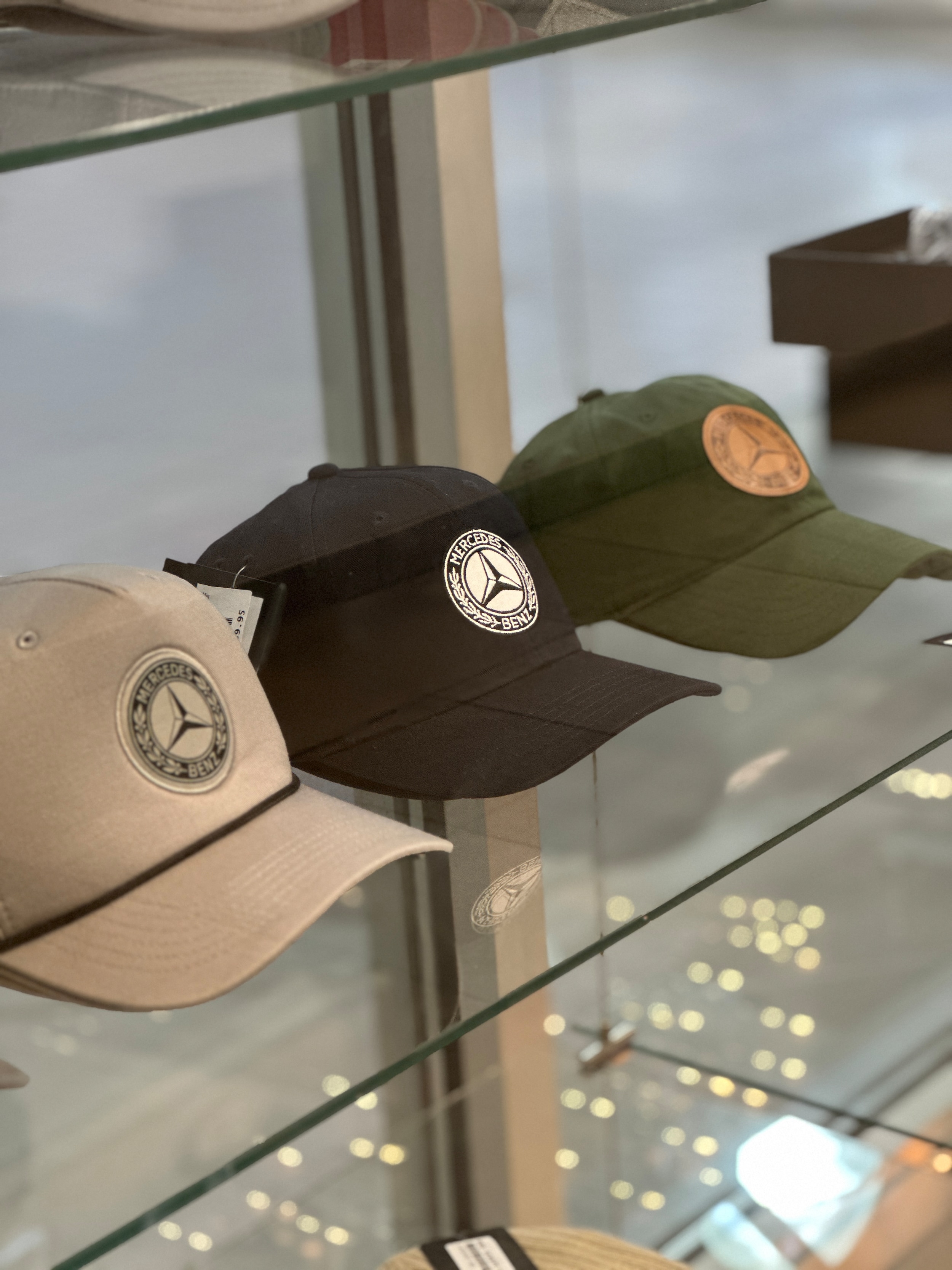 Mercedes-Benz hats in beige black and green displayed on glass shelves